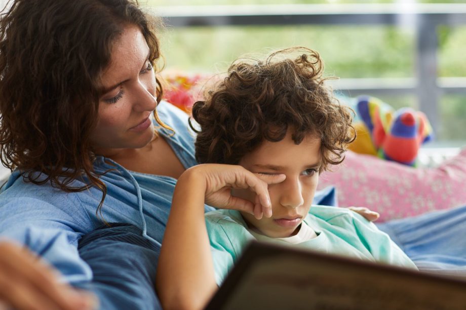 En mamma och hennes son sitter i en soffa och läser. Pojken kliar sig i ögonen, vilket är ett vanligt symtom på pollenallergi.